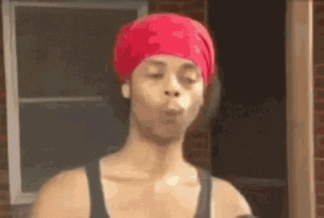 a woman wearing a red headband and a black tank top is blowing a bubble .
