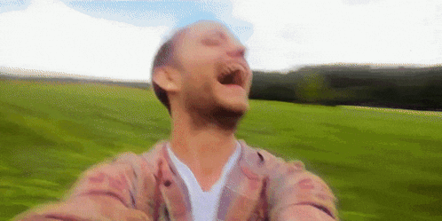 a man in a plaid shirt is laughing in a grassy field