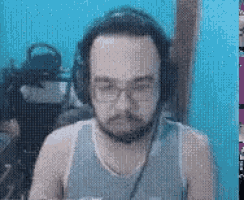 a man with a beard wearing headphones and a tank top is sitting in front of a blue wall .