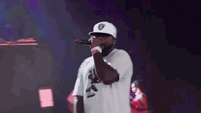 a man singing into a microphone wearing a white raiders hat