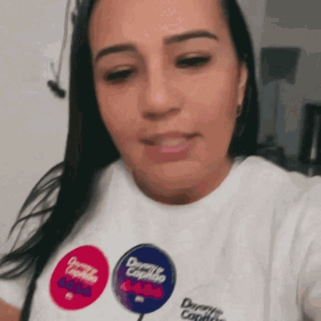 a woman wearing a white t-shirt with three stickers on it is taking a picture of herself .