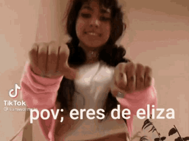 a girl in a pink sweater is giving a thumbs up and says `` pov , eres de eliza '' .