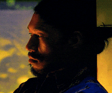 a man with a beard is leaning against a wall and looking out the window