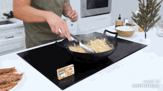 a man is stirring noodles in a wok on a stove top with a box of ranch dressing in the background