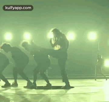 a group of people are dancing on a stage with lights behind them .