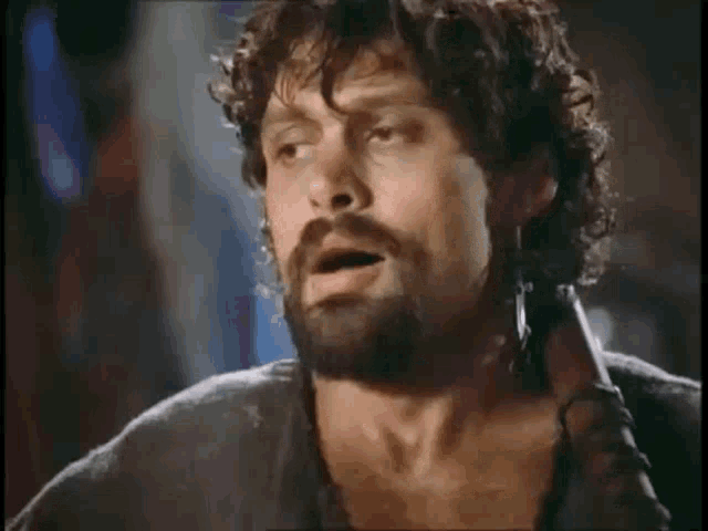 a man with curly hair and a beard is holding a sword in his hand .