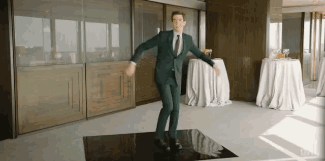 a man in a suit and tie is dancing on a black dance floor in a room .
