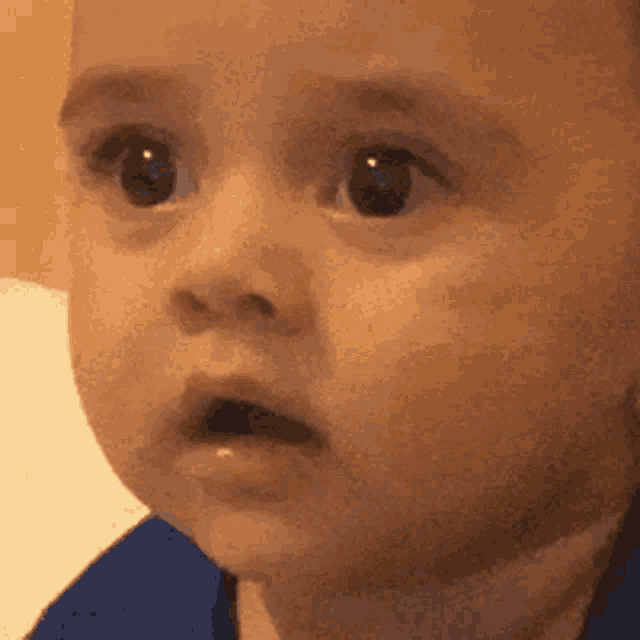 a close up of a baby 's face with his mouth open and a surprised look on his face .