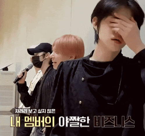 a man covering his face with his hand while another man sings behind him
