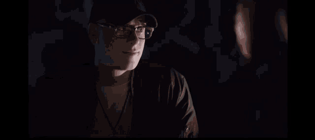 a man with glasses and a hat is talking to another man in a dark room .