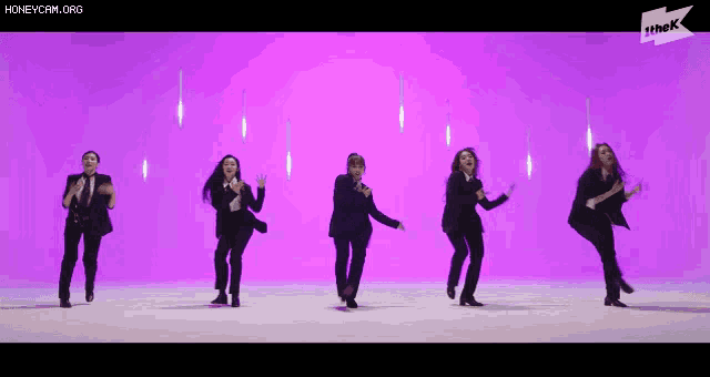 a group of women in suits are dancing together on a purple background .