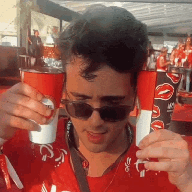 a man wearing sunglasses and a red shirt is drinking from a red cup that says camel