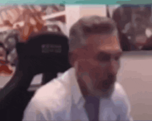 a man with gray hair and a beard is sitting in a chair with his mouth open .