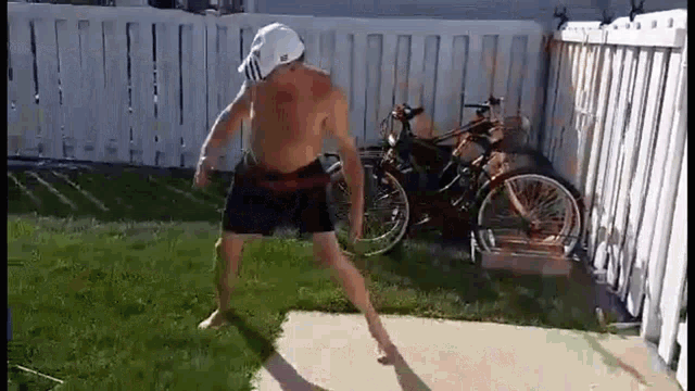 a shirtless man is dancing in a backyard in front of a fence and bikes .