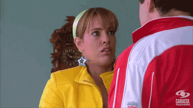 a woman in a yellow jacket is talking to a man in a red and white jacket with caracol television written on the sleeve