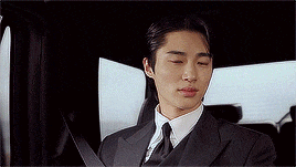 a man in a suit and tie is sitting in the back seat of a car with his eyes closed .