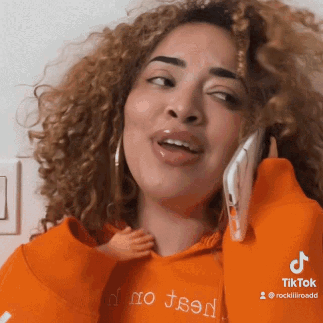 a woman talking on a cell phone while wearing an orange hoodie that says " no teen "