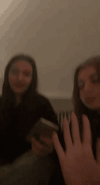 two girls are sitting next to each other in a dark room and one of them is holding a cell phone