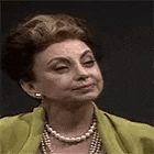 a woman wearing a green jacket and a pearl necklace is smiling .