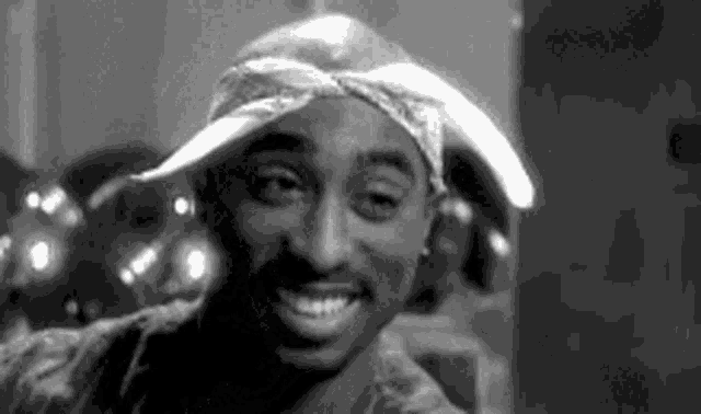 a black and white photo of tupac shakur wearing a bandana and a hat .