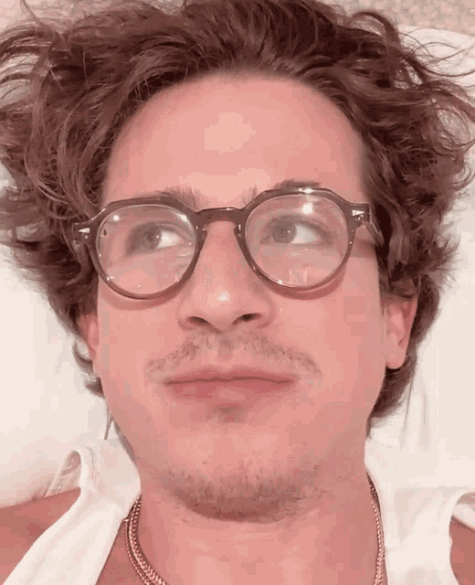 a man wearing glasses and a necklace looks at the camera