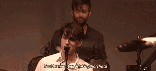 a man is playing drums and singing into a microphone while another man plays drums .