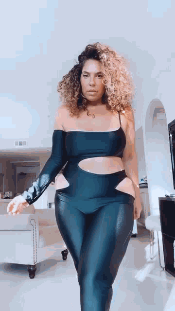 a woman with curly hair is standing in a living room wearing a black bodysuit .