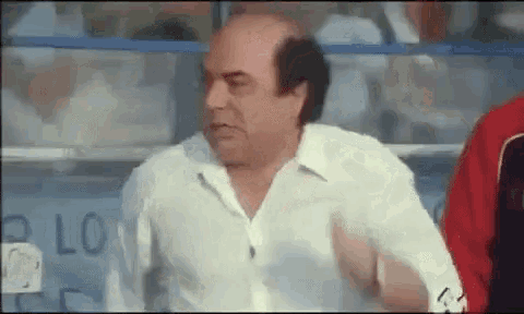 a bald man in a white shirt is standing in front of a sign that says ' lo ' on it .