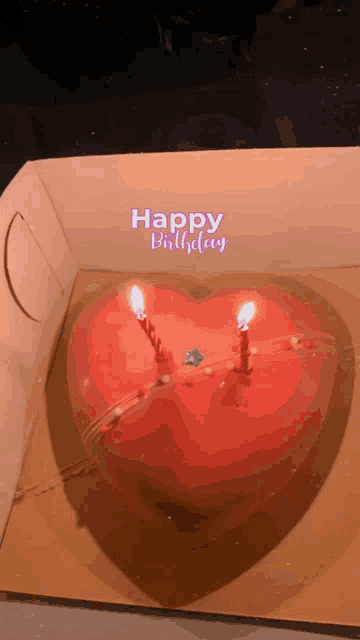 a heart shaped birthday cake with two lit candles in a box that says " happy birthday "