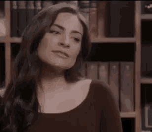 a woman is smiling in front of a bookshelf with books on it .