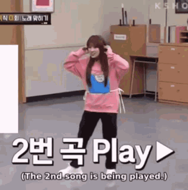 a girl in a pink sweatshirt is dancing in front of a sign that says play on it