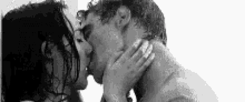 a black and white photo of a man and woman kissing in a shower .