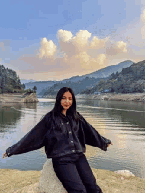 a woman is sitting on a rock in front of a lake .