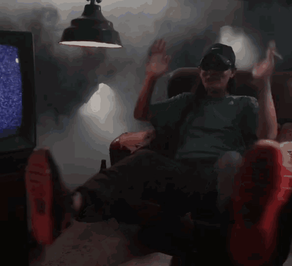 a man wearing sunglasses and a hat is sitting in front of a tv