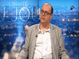 a man in a suit is sitting in front of a screen that says l' invite jour