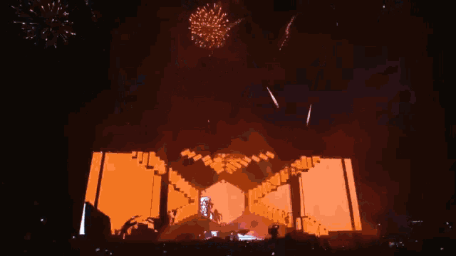 fireworks are displayed over a stage with a large orange screen