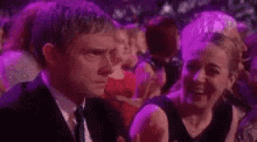 a man in a suit and tie is sitting next to a woman in a crowd .