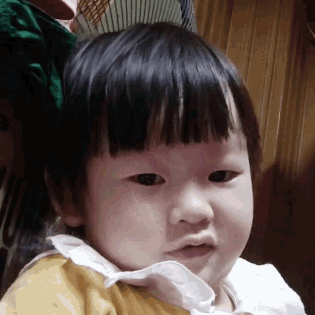 a baby girl wearing a yellow shirt and a white collar is making a funny face .