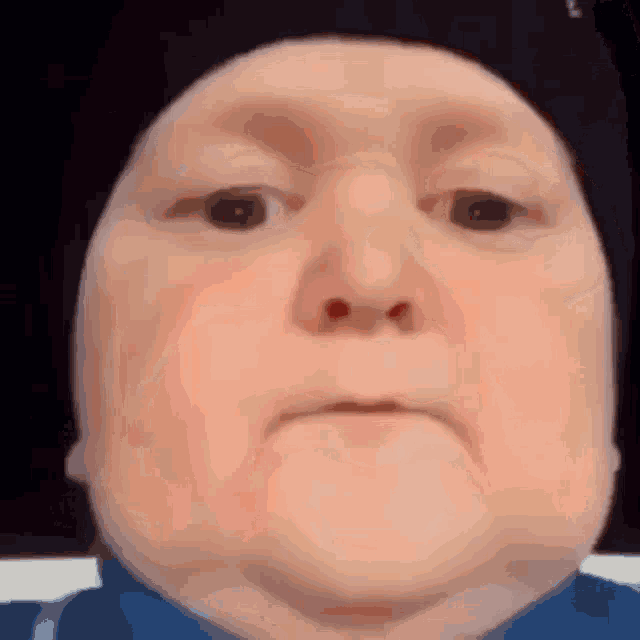 a close up of a person 's face with a hat on and a blue shirt .