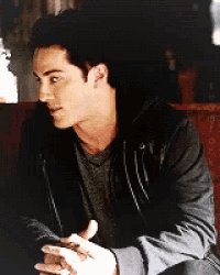 a man in a grey shirt and black jacket is sitting down