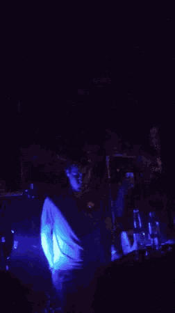 a man in a dark room with a blue light behind him and a bottle of jack daniels on the table