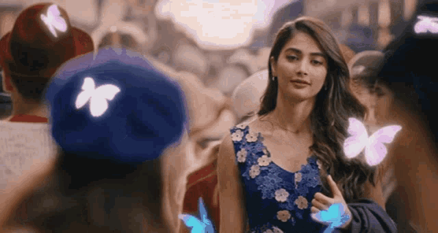 a woman in a blue dress stands in a crowd of people with butterflies flying around her