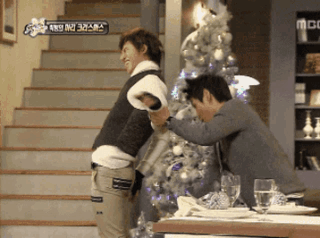 two men are standing in front of a christmas tree and a sign that says mbc on it