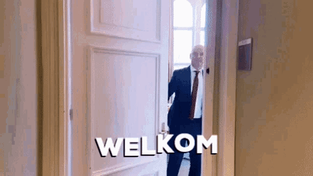 a man in a suit and tie is opening a door that says welkom on it