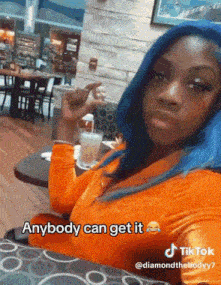 a woman with blue hair is sitting at a table with a drink in her hand and the caption anybody can get it on the bottom