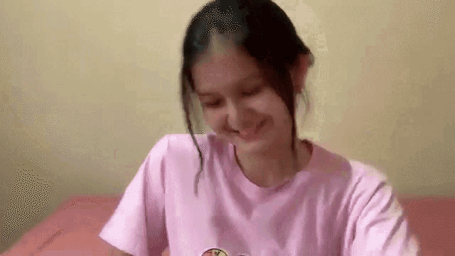 a woman in a pink shirt is sitting on a bed .