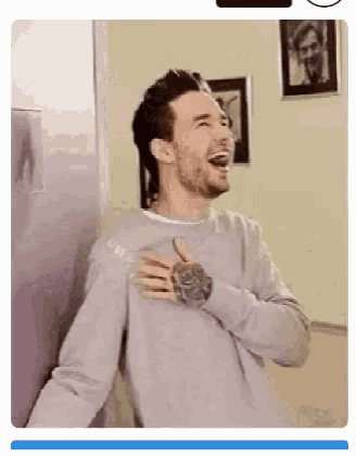 a man is laughing with his hands on his chest while standing next to a wall .
