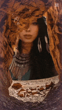 a woman in a native american outfit is looking out of a rocky cave