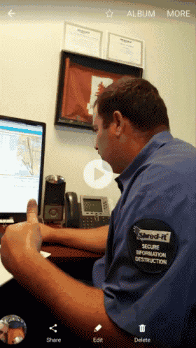 a man wearing a shred-it secure information destruction shirt is sitting at a desk