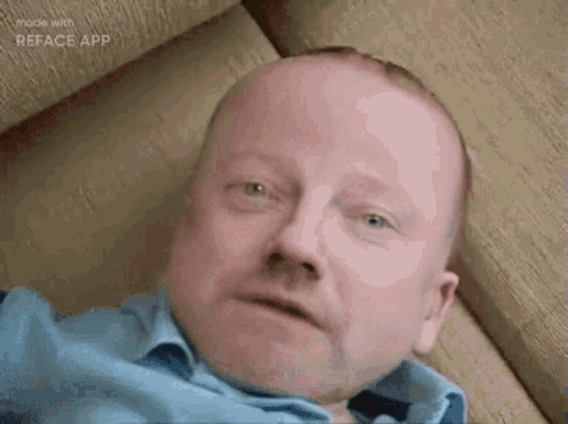 a man in a blue shirt is laying on a couch and looking at the camera .